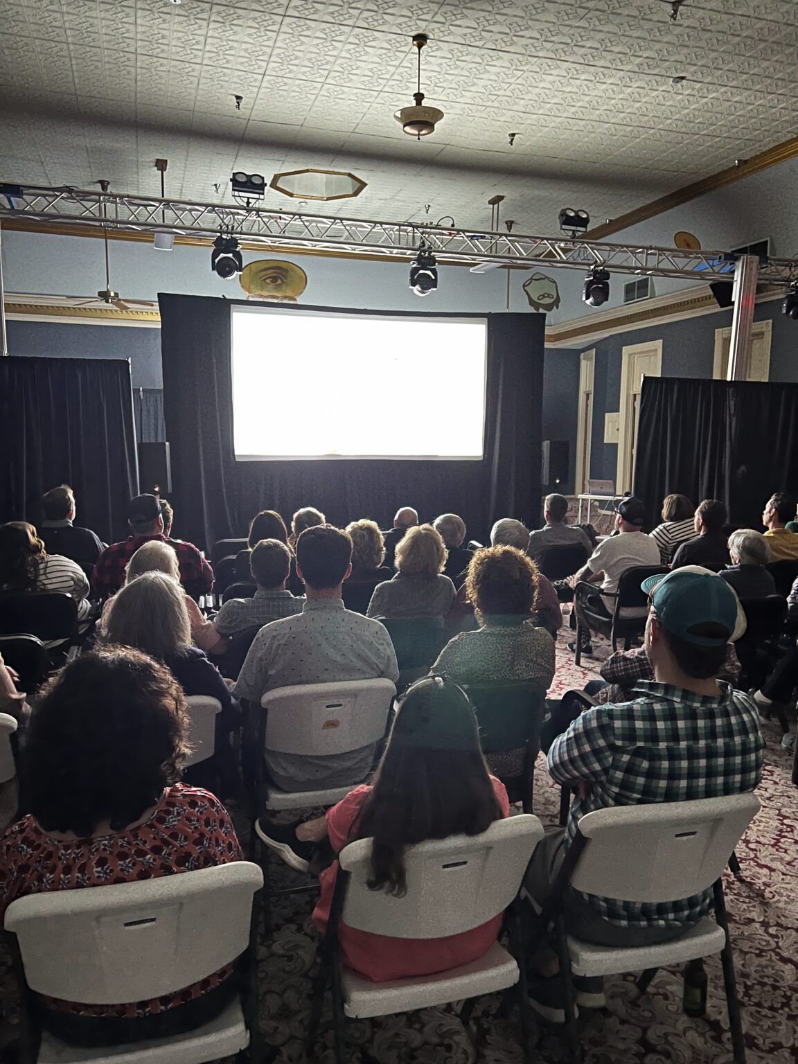 An audience seated in folding chairs watching a film at the IOOF Hall